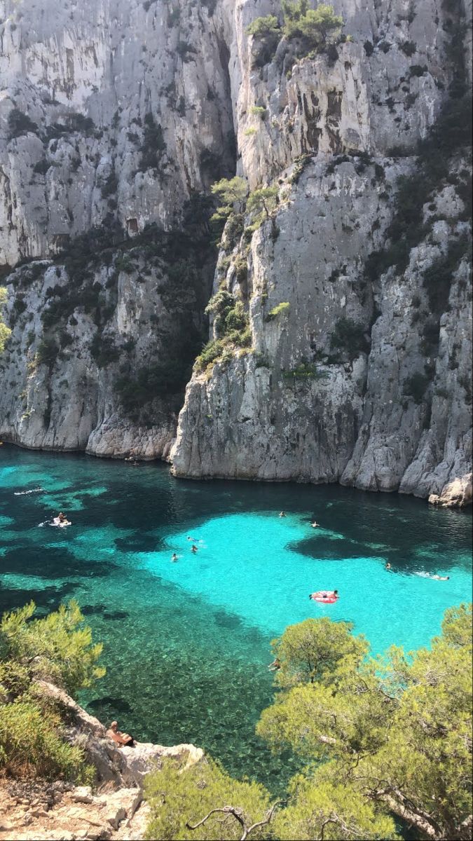 people are swimming in the clear blue water near some cliffs and trees on either side