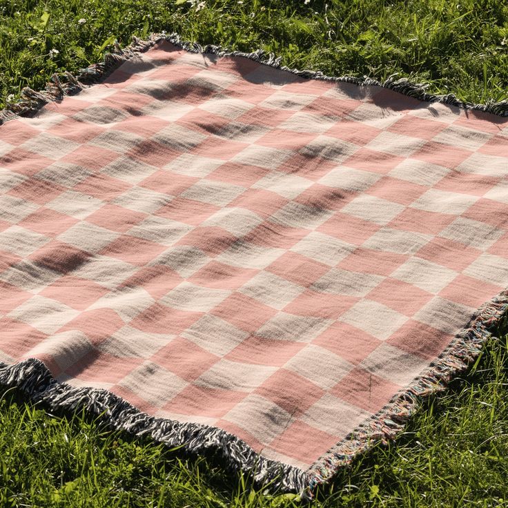 a pink and white checkered blanket laying in the grass