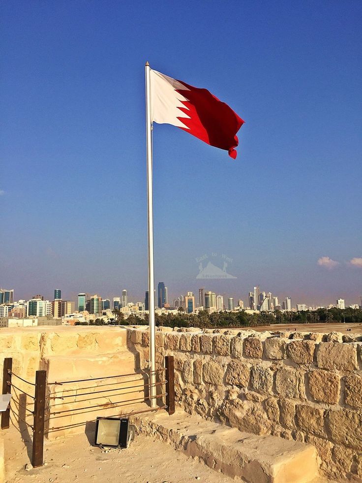 a flag flying in the air next to a stone wall with a cityscape in the background