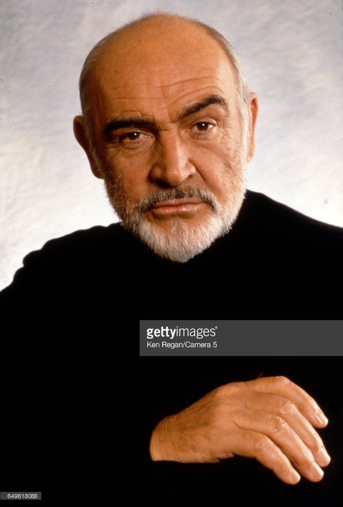 an older man with white hair wearing a black shirt and holding his arms crossed in front of him