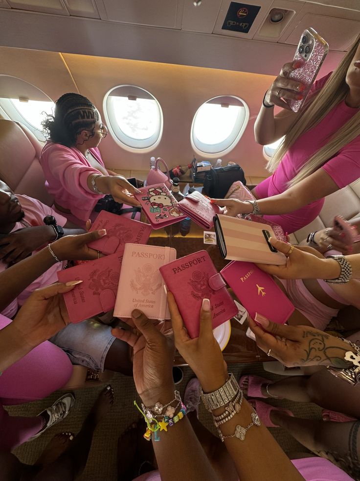 several women in pink shirts and bracelets are sitting on an airplane with their hands together