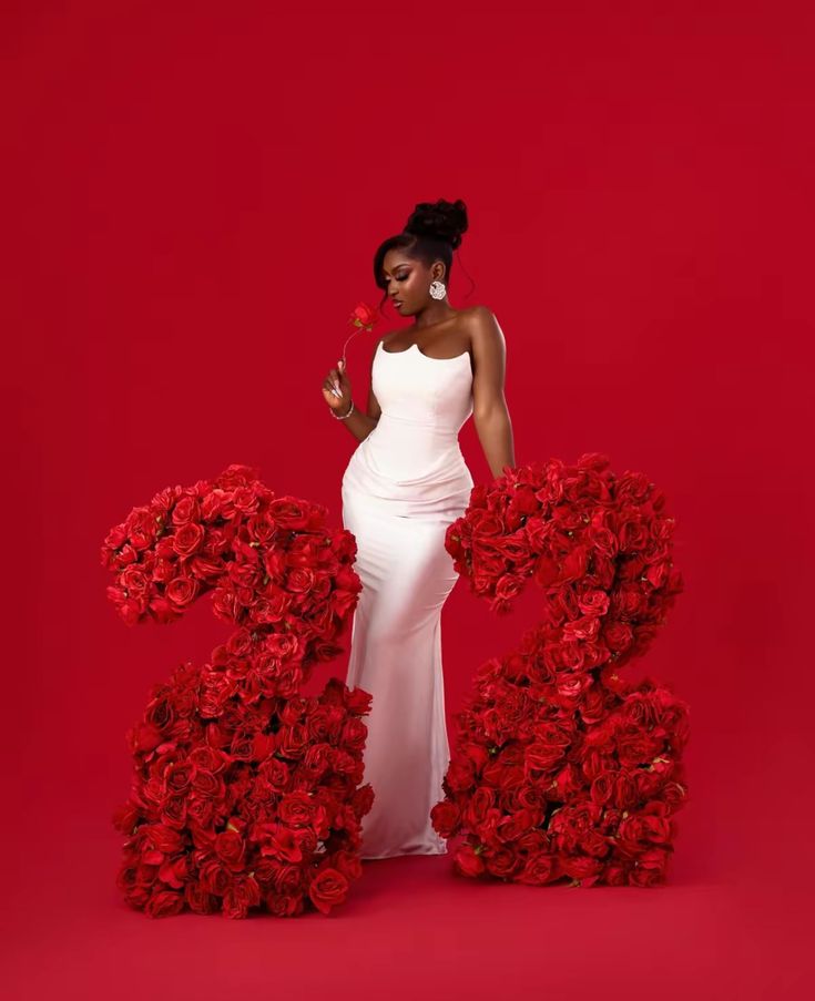 a woman in a white dress is standing next to red flowers and the letter b