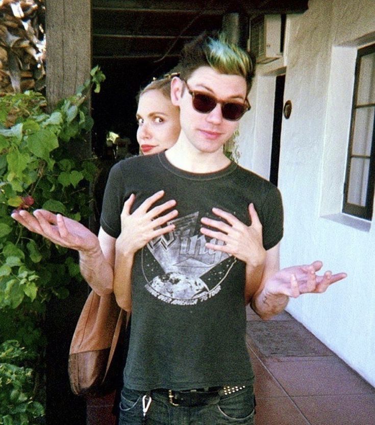 a man and woman standing in front of a house with their hands out to each other