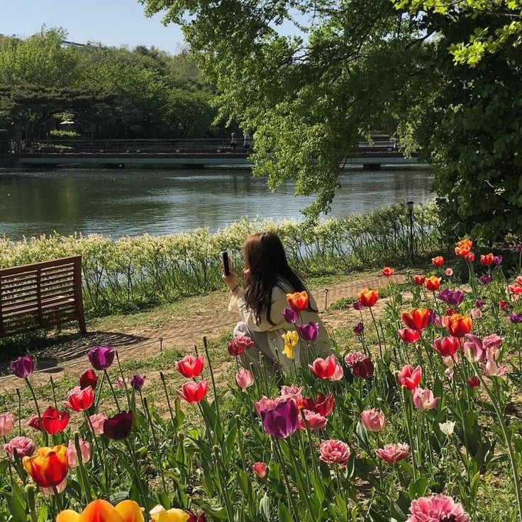 a woman sitting on a park bench next to a field of tulips and other flowers