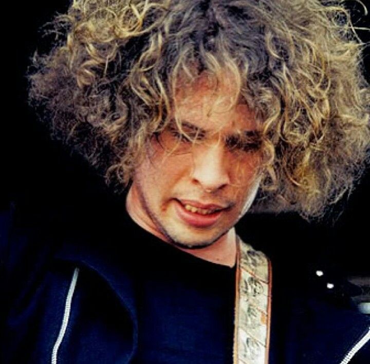 a close up of a person with curly hair holding a guitar and looking at his cell phone