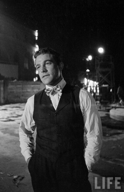 black and white photograph of a man wearing a bow tie standing in the street at night