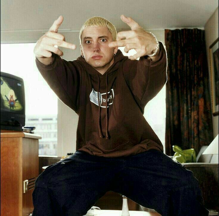 a young man sitting on top of a bed giving the thumbs up sign with both hands