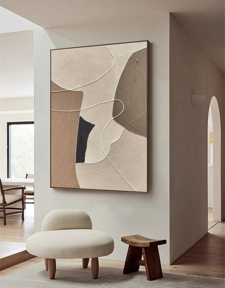 an abstract painting hangs on the wall next to a white chair and footstool