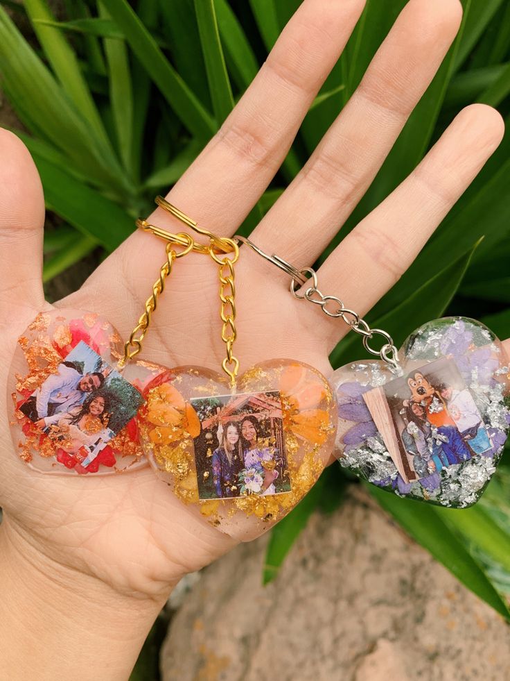 a hand holding three heart shaped key chains with pictures on them and two hearts in the middle