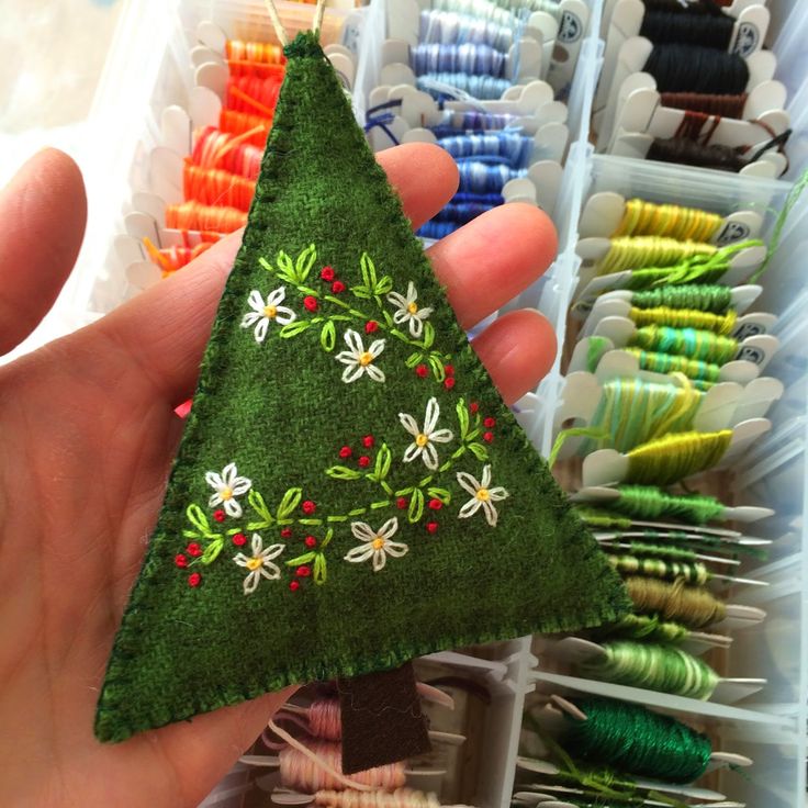 a hand holding a small green christmas tree ornament in front of many spools of thread