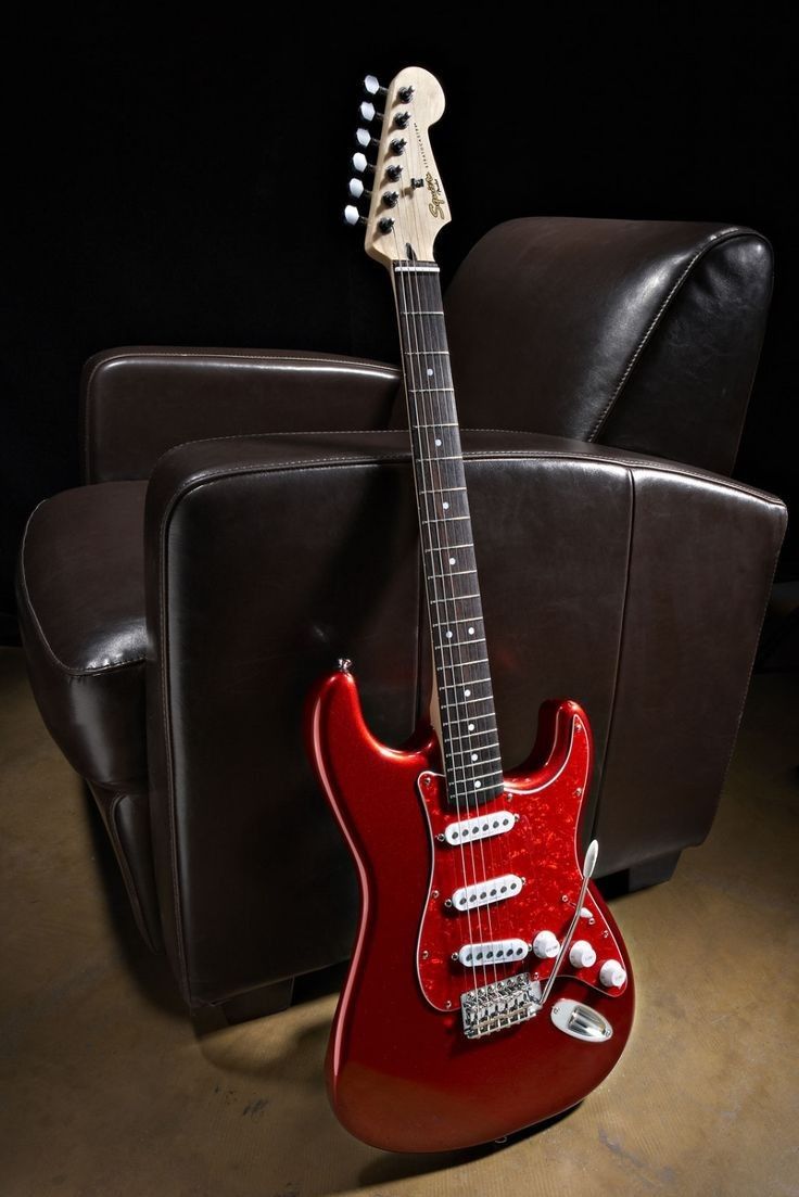 a red guitar sitting on top of a hard wood floor next to a black chair