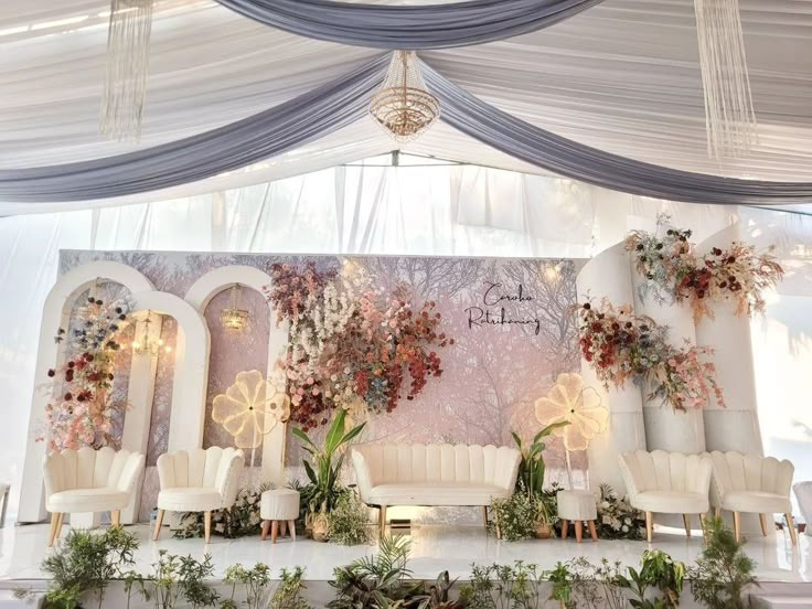 a stage set up with white chairs and floral decorations on the wall behind it for an event