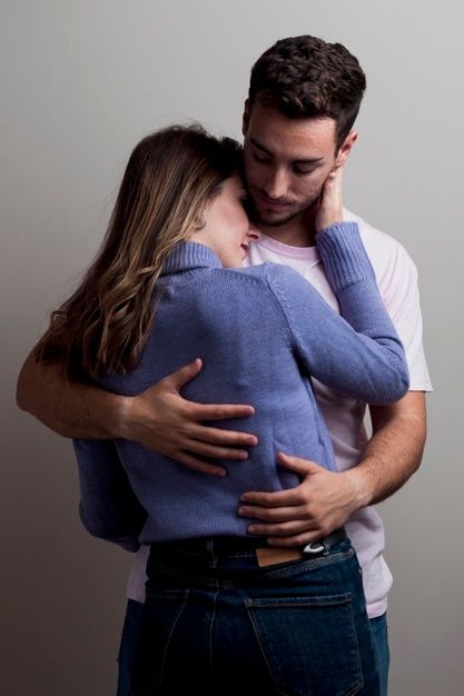 a man and woman embracing each other in front of a gray background with their arms around one another