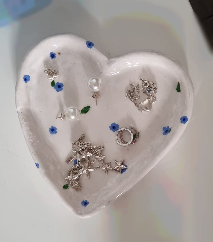 a white heart shaped dish with blue flowers and silver rings on the inside, sitting on a table