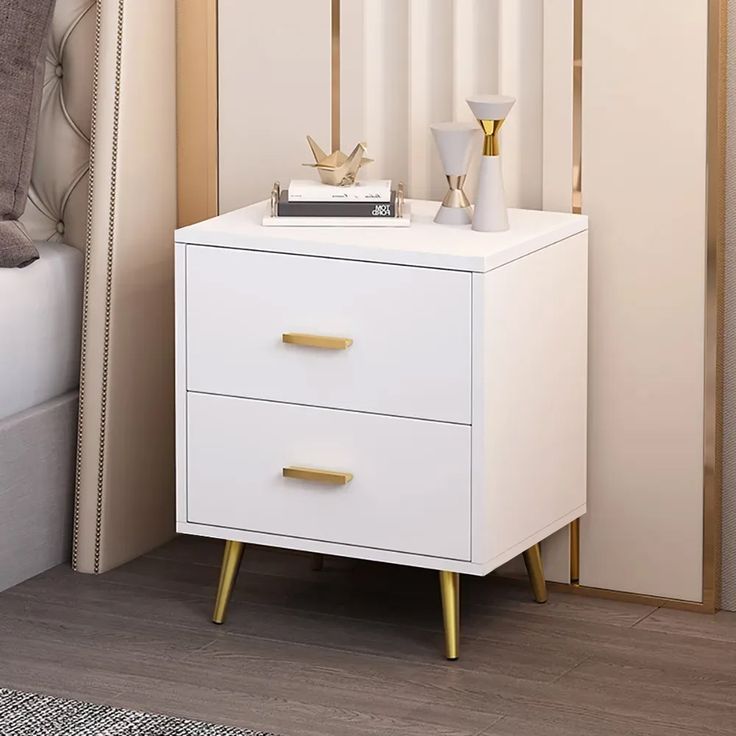 a white night stand with two gold handles on it in a bedroom next to a bed