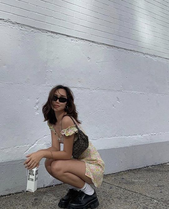 a woman squatting on the ground next to a white wall with a newspaper in her hand