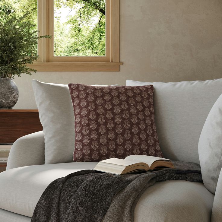 an open book is sitting on the arm of a white couch in front of a window