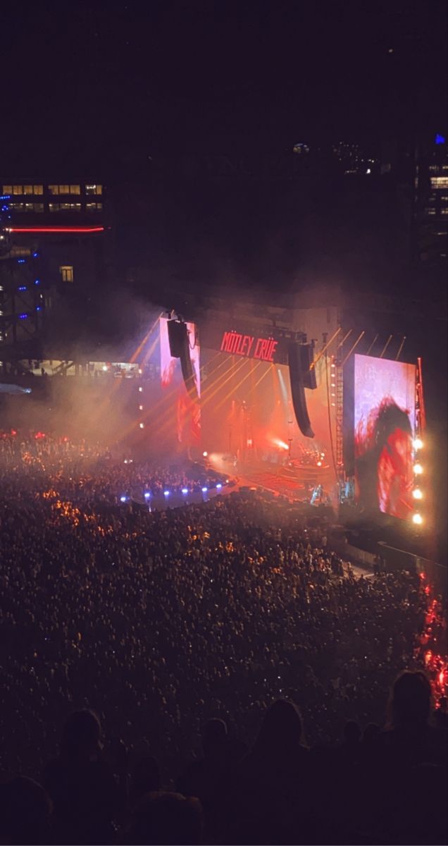 an outdoor concert is shown at night with lights on the stage and large crowd watching