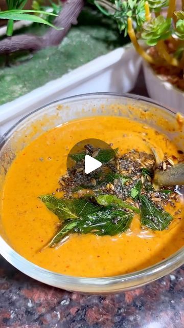 a glass bowl filled with carrot soup and garnished with green leafy toppings