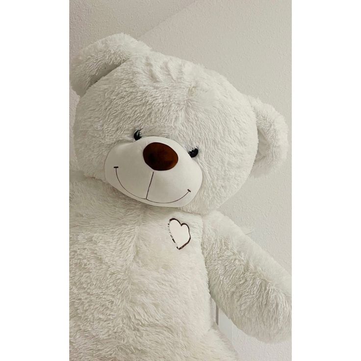 a large white teddy bear with a heart on it's chest sitting against a wall