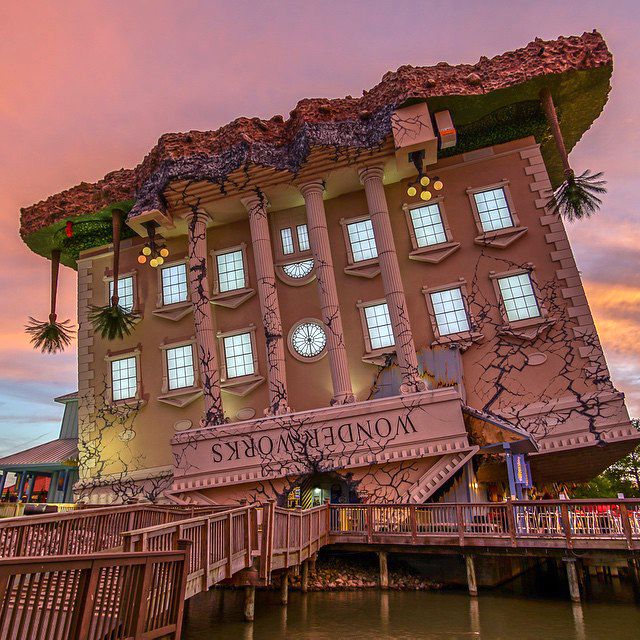 a large building that is on the side of a body of water in front of a pink sky