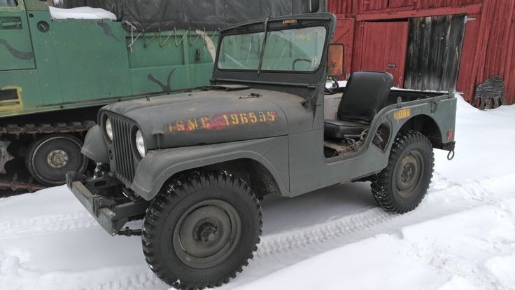 an old army jeep parked in front of a red barn with snow on the ground