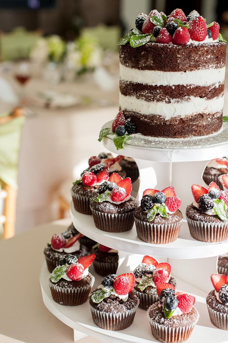 a triple layer cake and cupcakes are arranged on a white platter with fresh berries