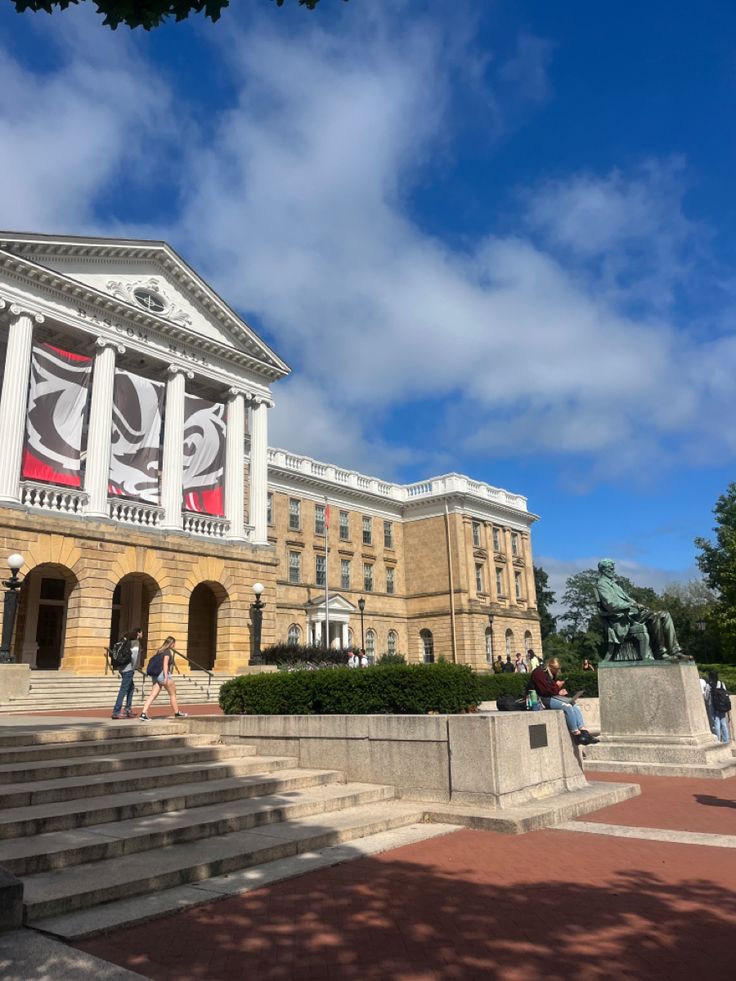 people walking in front of a large building with columns and flags on the side walk