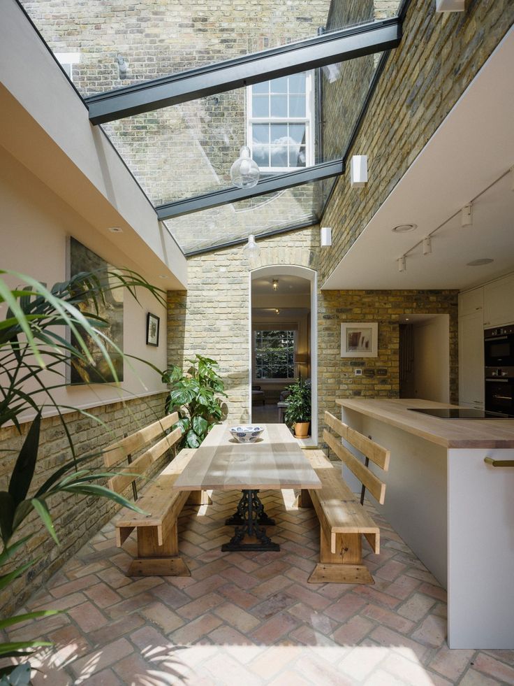 a long wooden table sitting under a skylight in a room with brick flooring