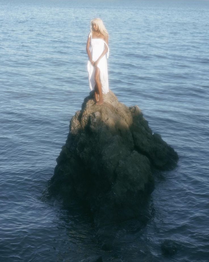 a woman standing on top of a rock in the ocean