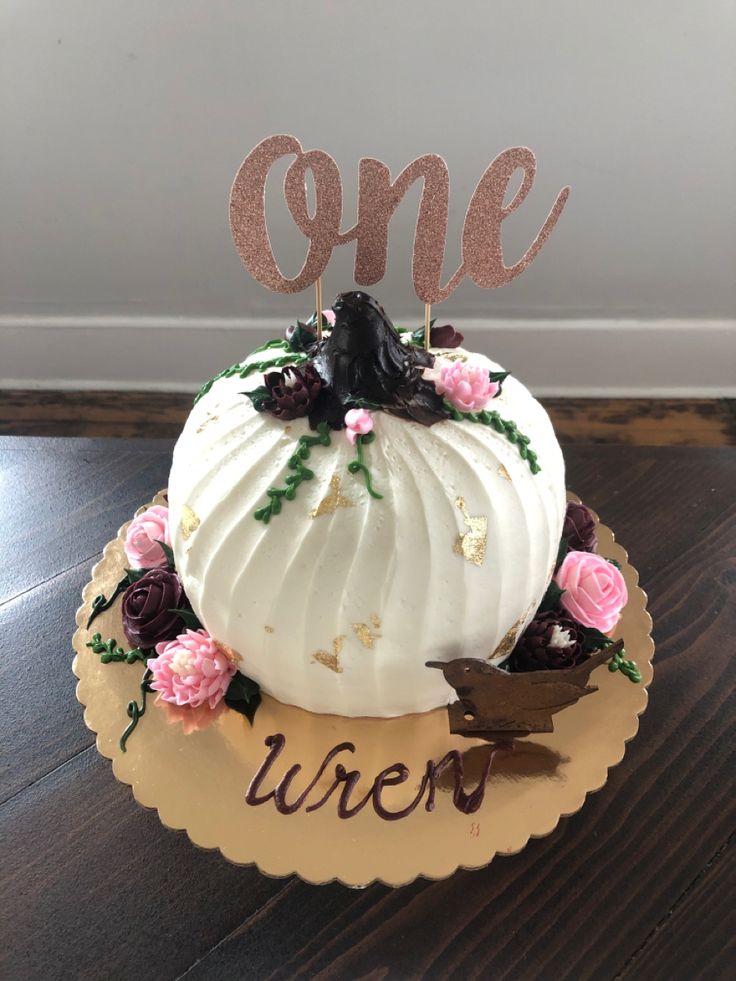 a white pumpkin decorated with pink flowers and the word one on top