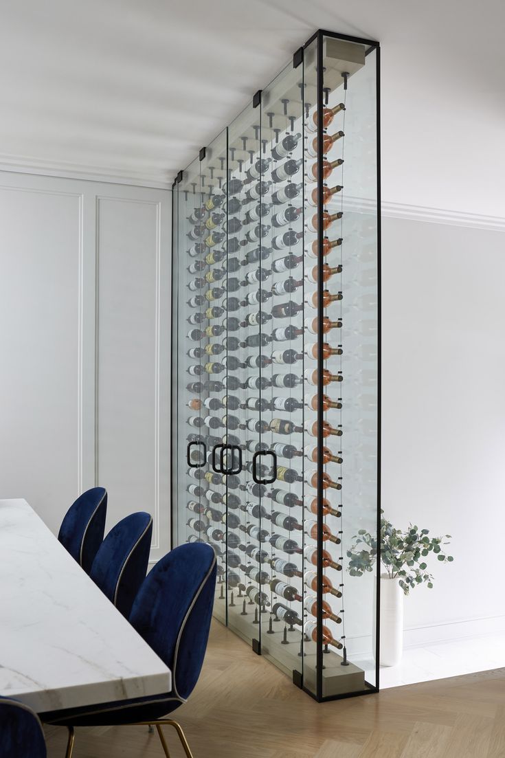 a dining room table with blue chairs in front of a wine rack filled with glasses