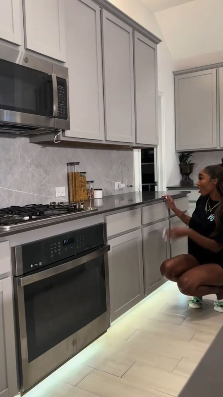 a woman kneeling down in a kitchen next to a stove top oven and microwave combination