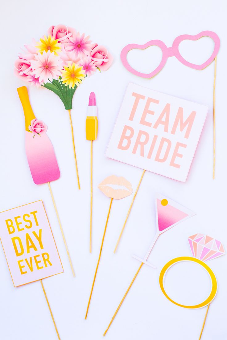 some pink and yellow items are on a white surface with flowers, sunglasses, lipstick, and cake toppers