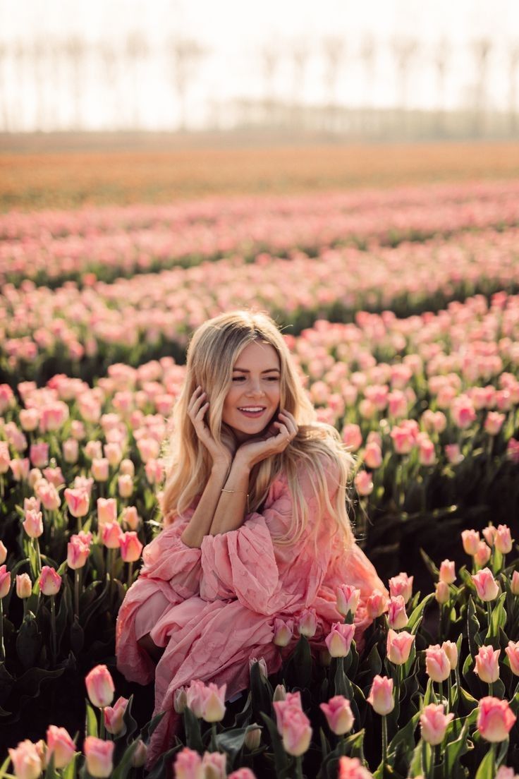 a woman in a pink dress sitting on top of a field of tulips