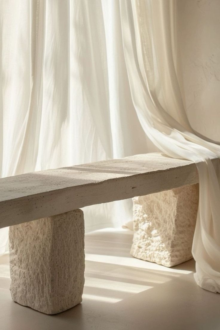 a stone bench sitting in front of a window with curtains on the windowsill behind it