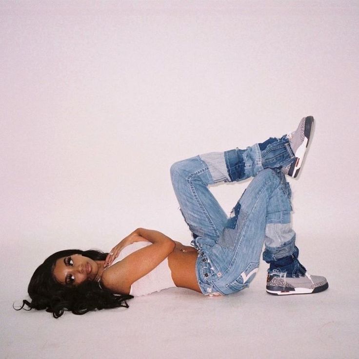 a woman laying on the ground with her legs crossed and wearing ripped jeans, white shirt and silver sneakers