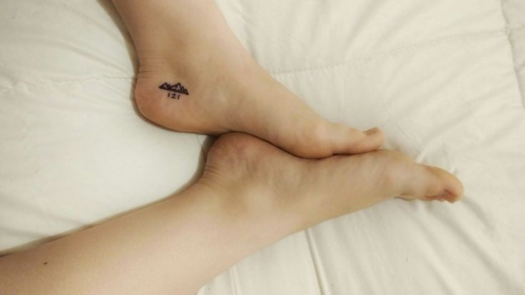 a person with a small tattoo on their foot laying in bed next to a pillow