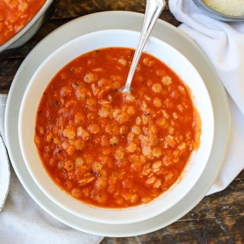 two bowls filled with soup on top of a wooden table next to silver spoons