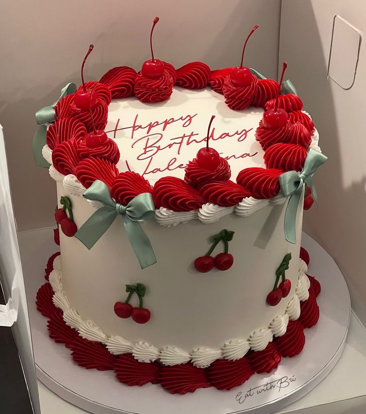 a white and red birthday cake with cherries on it