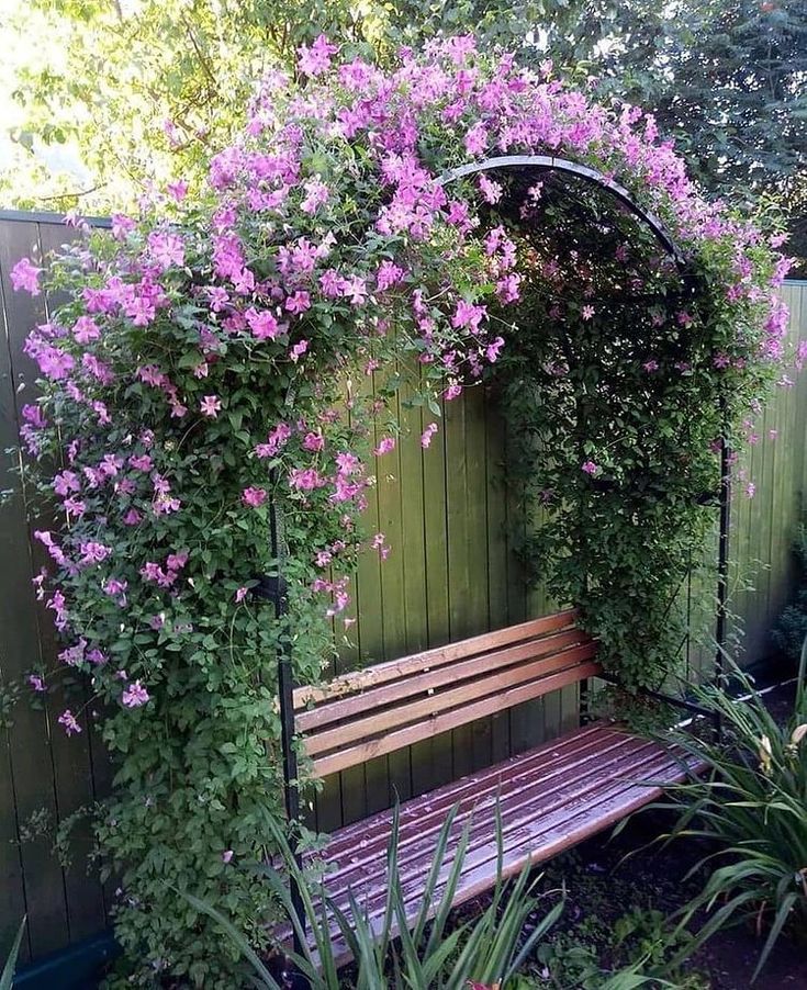 a wooden bench sitting under a purple flower covered arbor in the middle of a garden