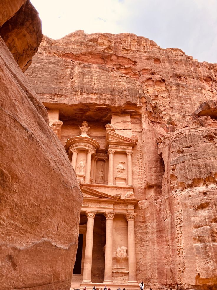 people standing in front of an ancient building carved into the side of a mountain