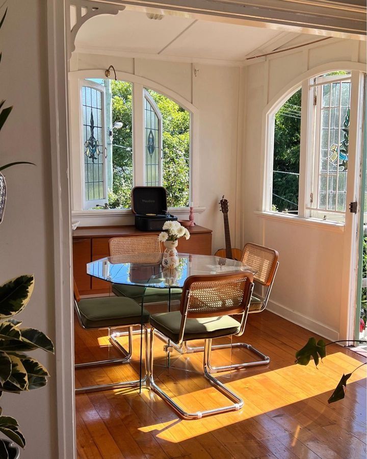 a dining room table with four chairs and a glass top in front of two windows