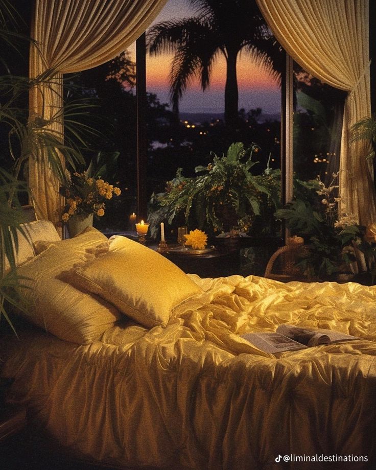 a bed with yellow sheets and pillows in front of a window at night, next to potted plants