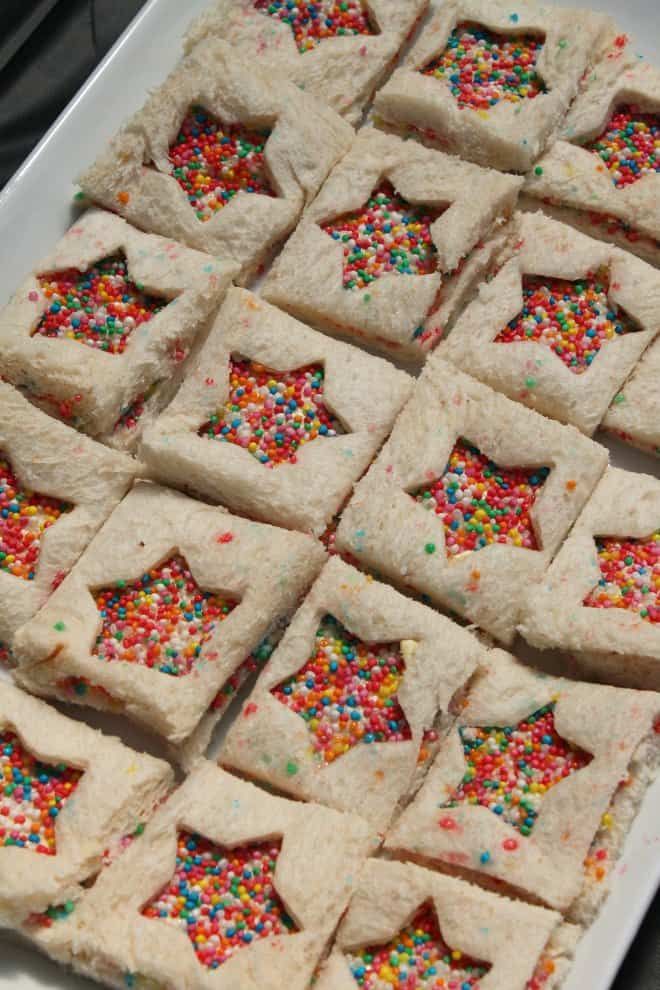 square shaped cookies with sprinkles are on a white platter, ready to be eaten