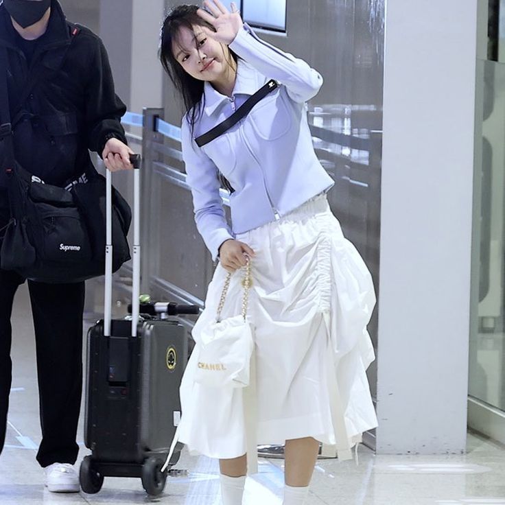 a woman in a white skirt is walking through an airport with luggage and a mask on her face