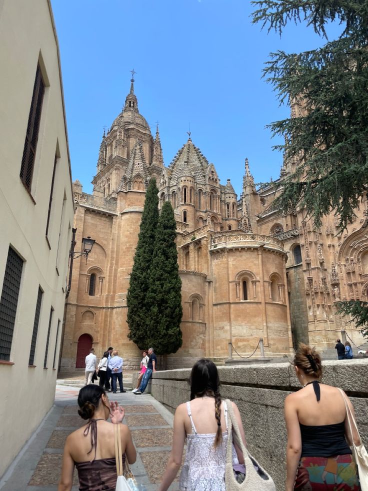 two women walking down the street in front of an old building with towers and spires