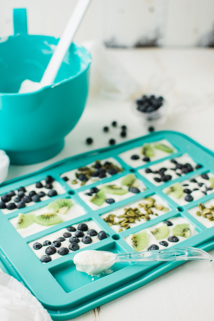 an ice tray with blueberries, kiwis and blackberries on it next to a spoon