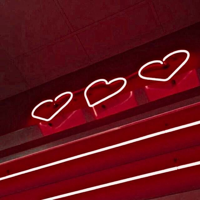 a neon sign with three hearts on it's side in front of a red wall