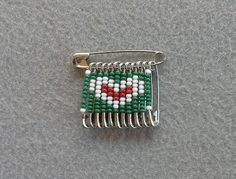 a green and white beaded comb with a heart on it's side, sitting on a gray surface